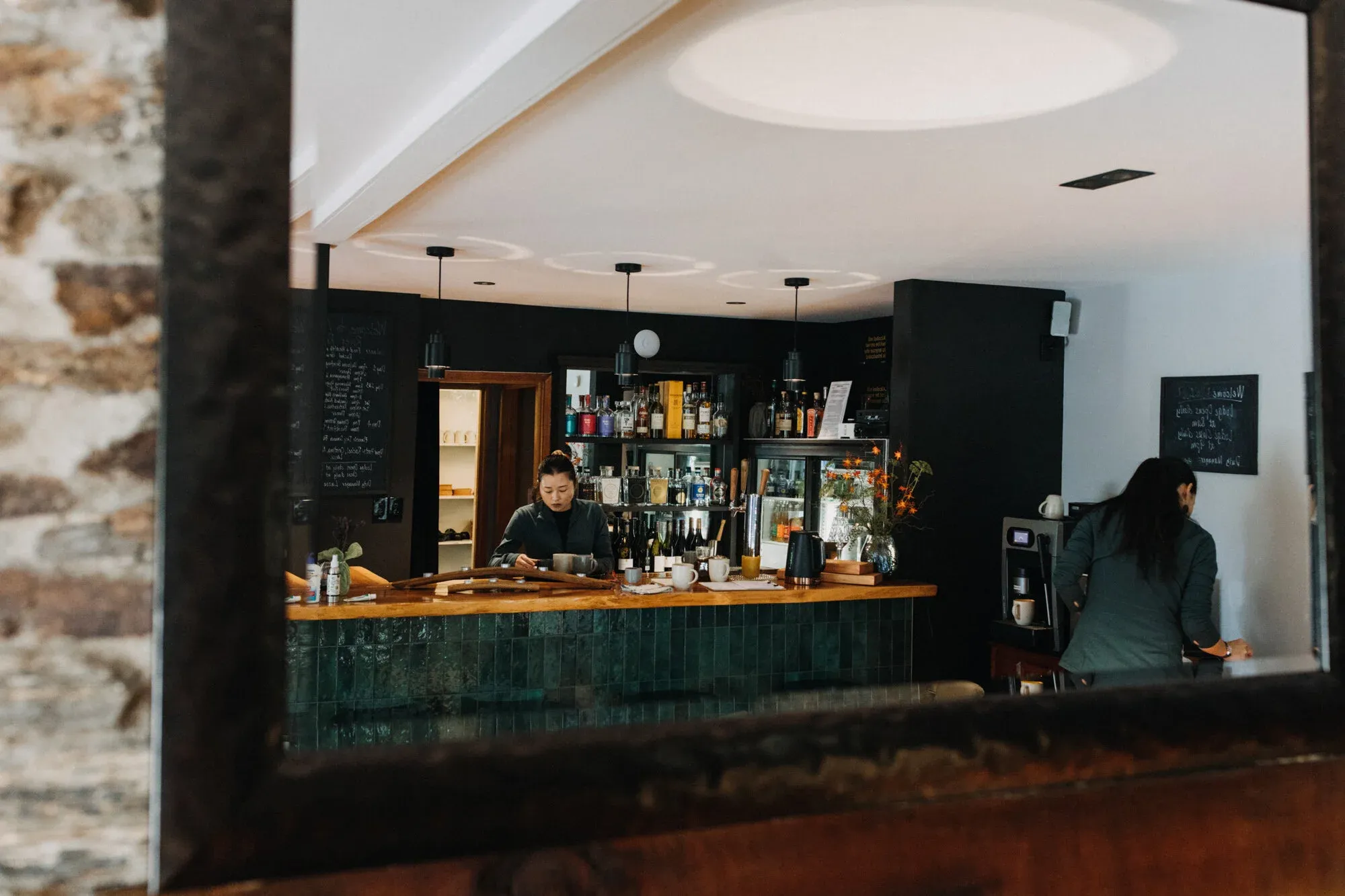 Bar area with a wooden counter, green tiles, and a barista preparing drinks behind a glass display.