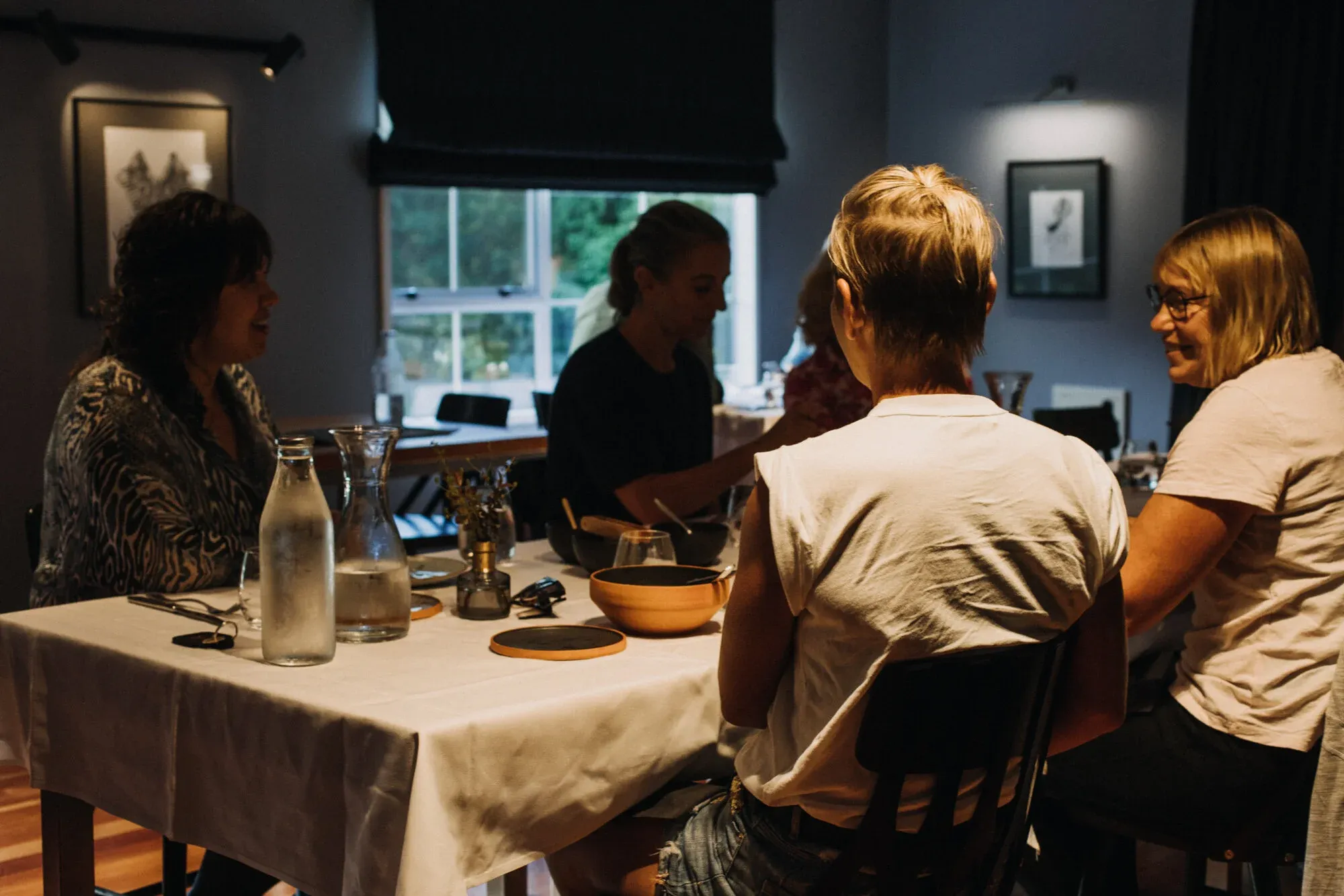 Guests seated around a table with a white tablecloth, water carafes, and bowls in a dimly lit dining area.