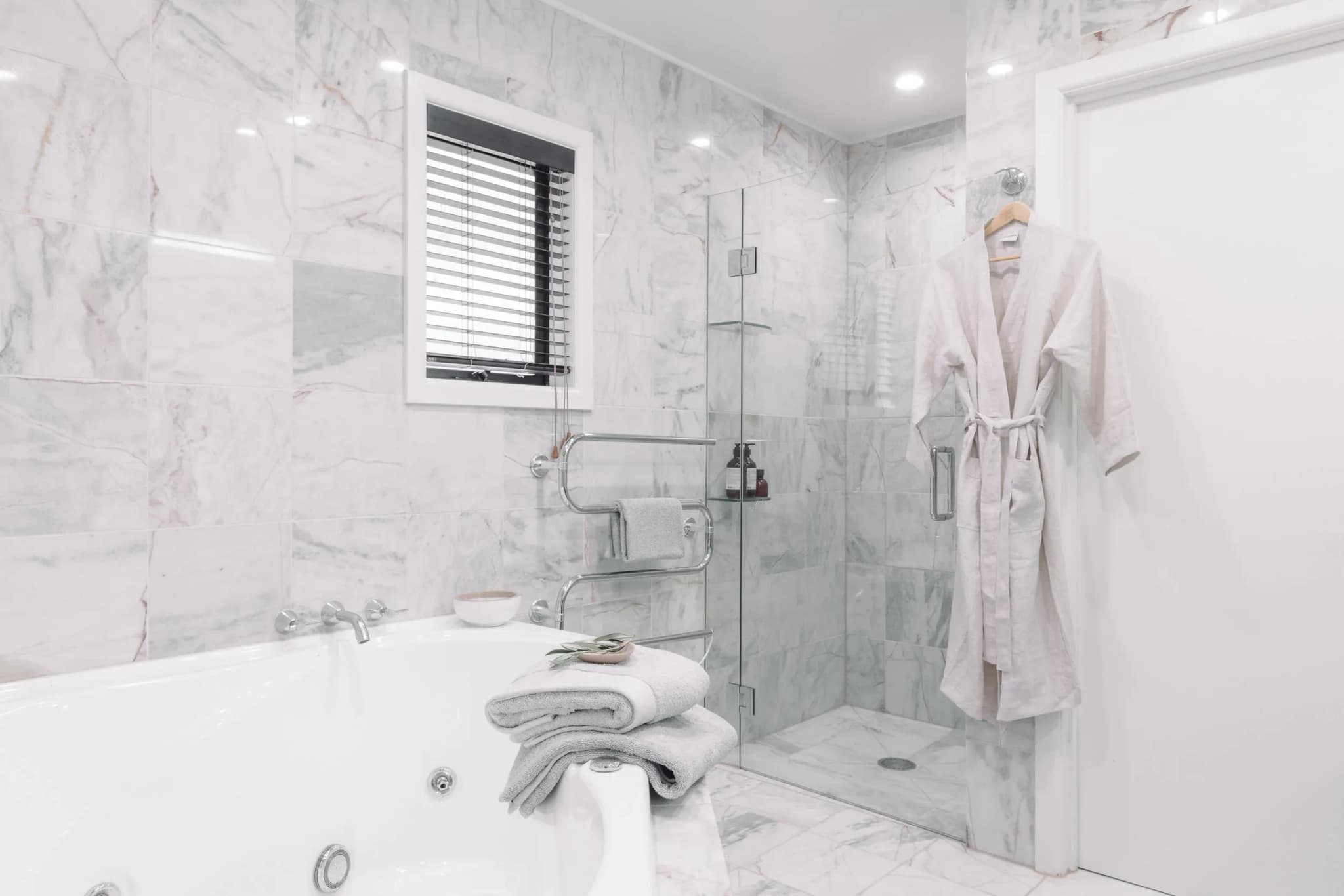 Marble bathroom featuring a freestanding tub, gray towels stacked, glass shower, and a light-colored robe hanging on the door.
