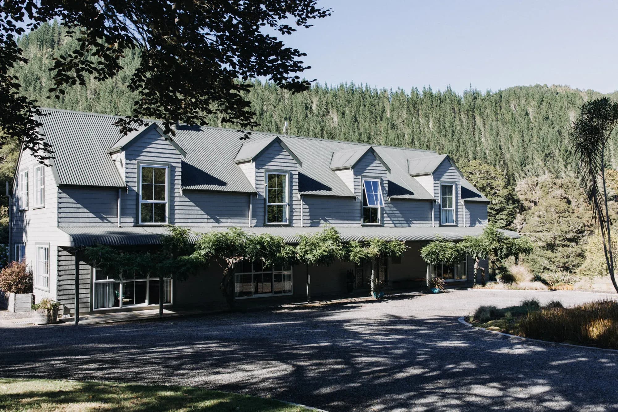 Timber-clad building with a sloped roof, large windows, and surrounding greenery at Maruia River Retreat.