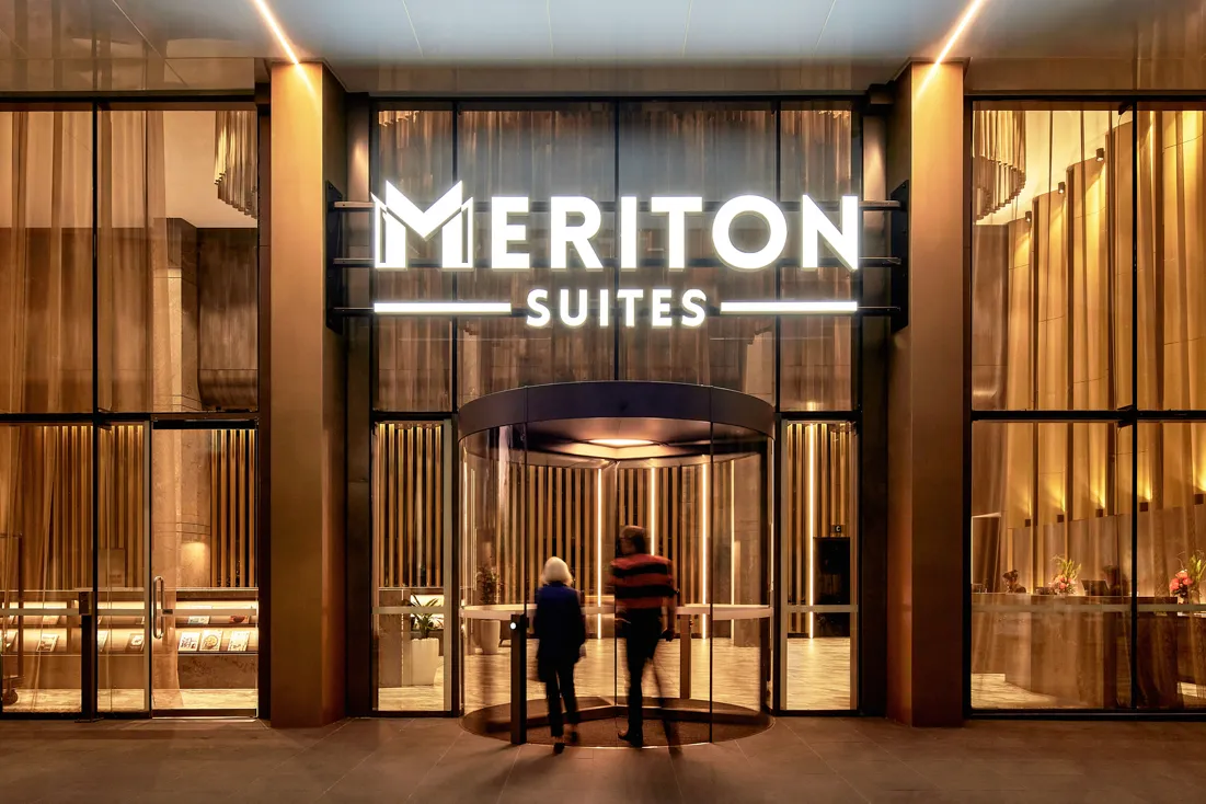 Entrance of Meriton Suites Canberra featuring a revolving door, large glass windows, and illuminated signage.