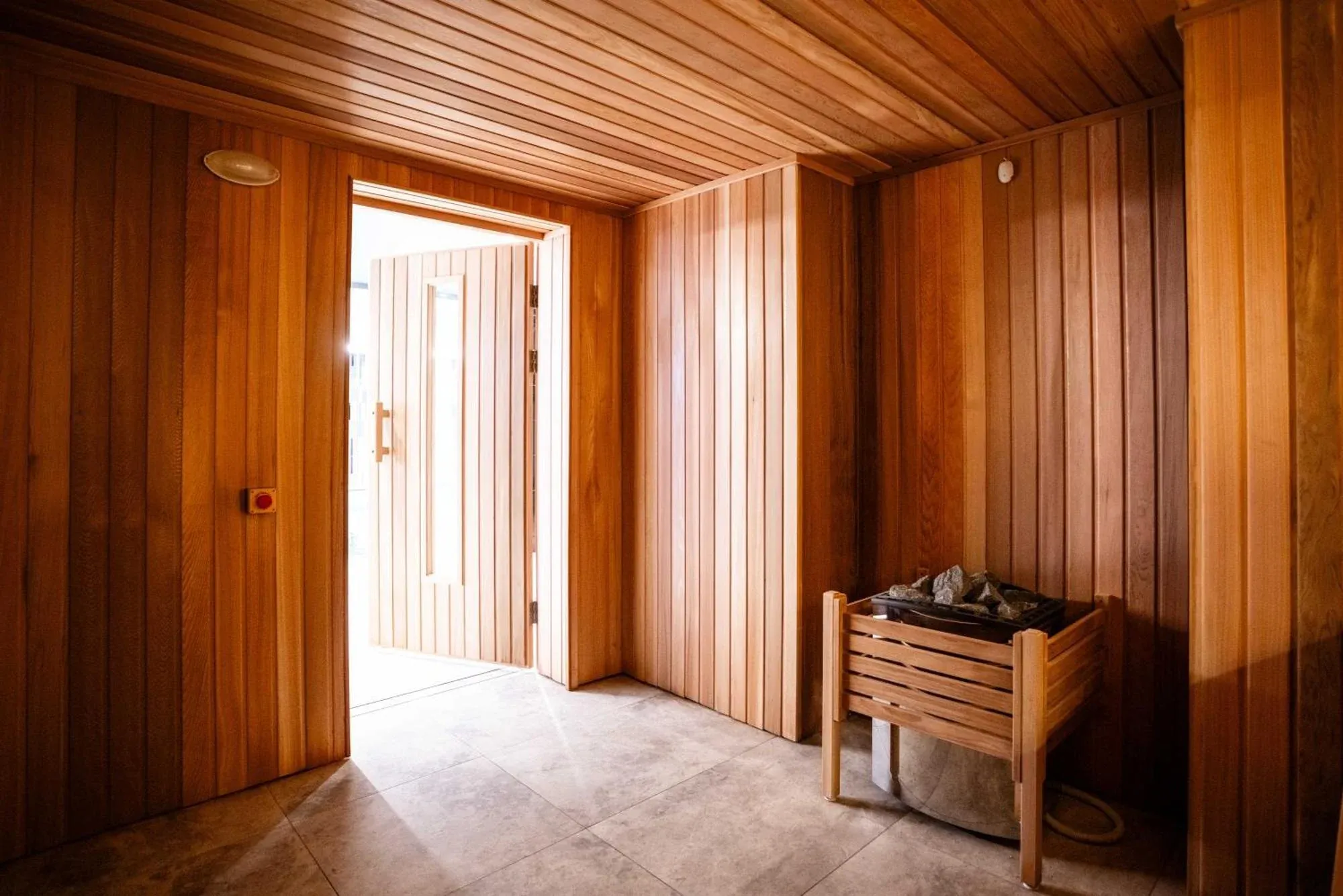 Sauna interior with wooden paneling, a stone heater, and an open door leading outside.