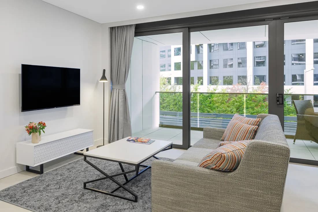 Living area with a grey sofa, modern coffee table, television, and sliding glass doors leading to a balcony.