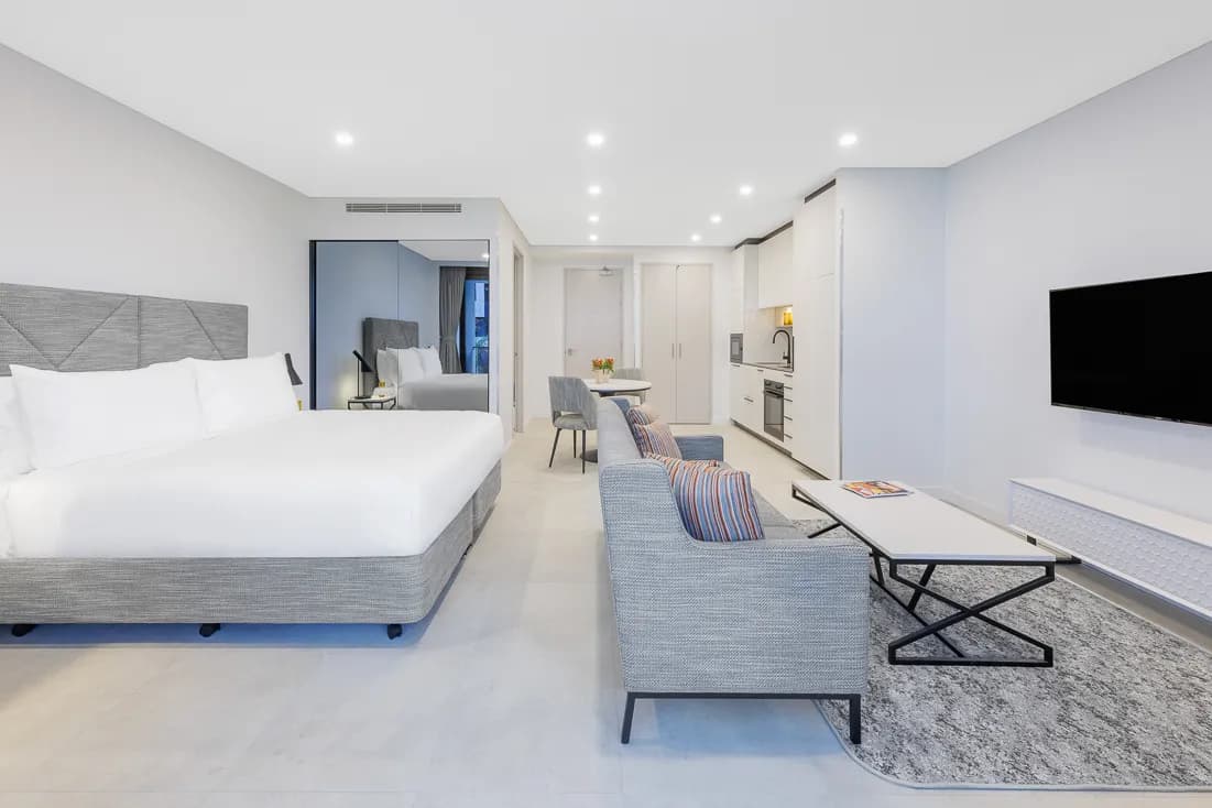 Modern suite featuring a king bed, sitting area, kitchenette, and flat-screen TV.
