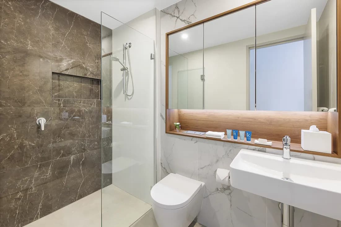 Bathroom interior featuring a glass shower, marble walls, and a wooden vanity with toiletries.