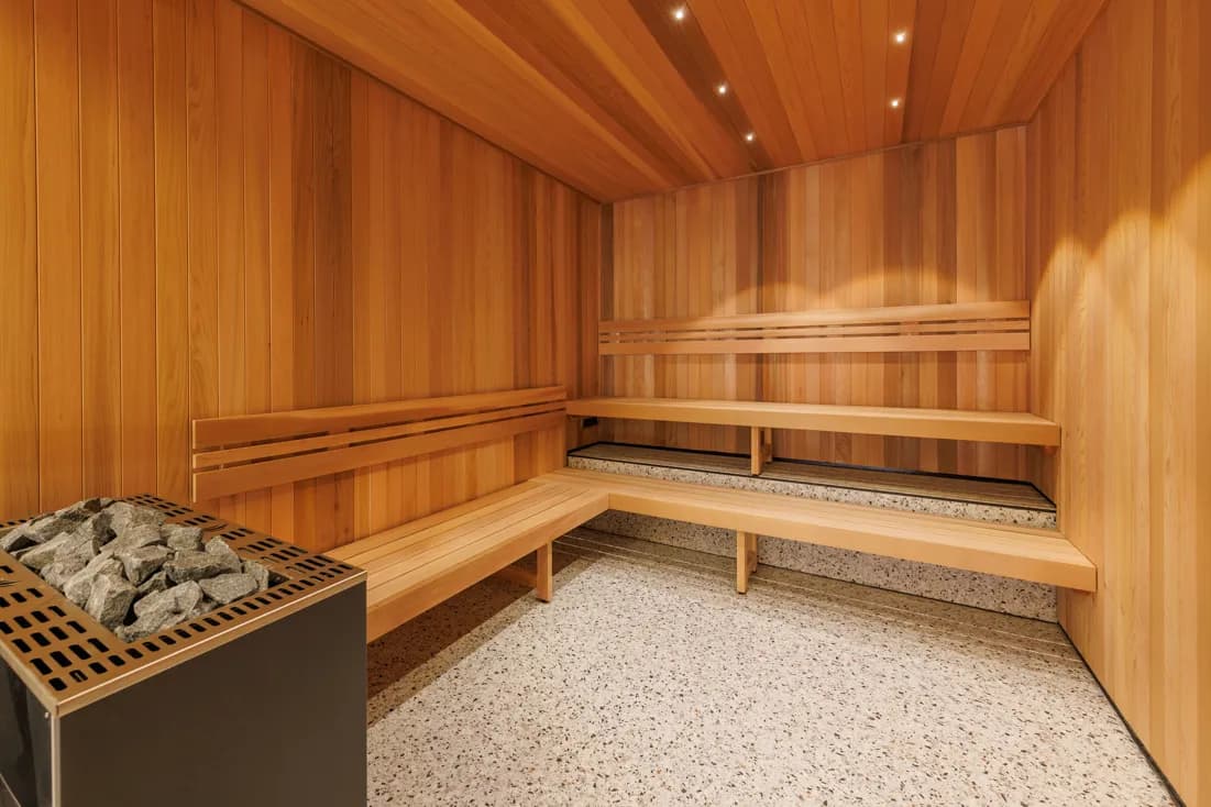Sauna interior featuring wooden paneling, wooden benches, a stone heater, and a speckled floor.