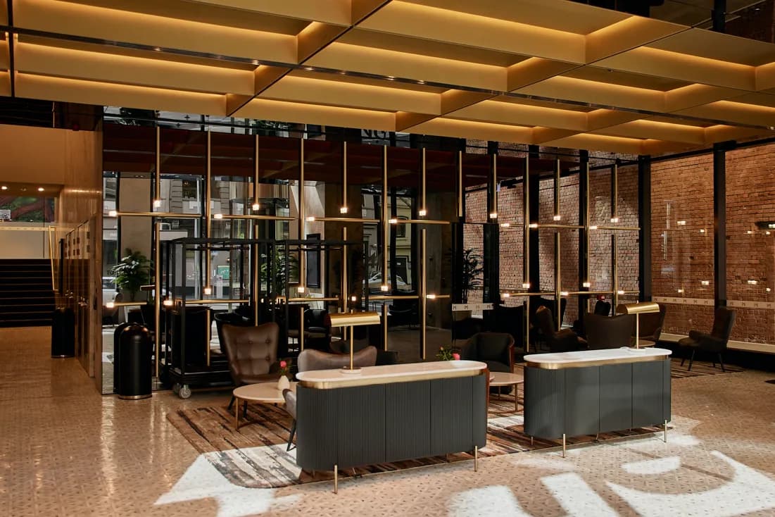 Lobby area with modern furnishings, including two reception desks, seating, plants, and a patterned floor.
