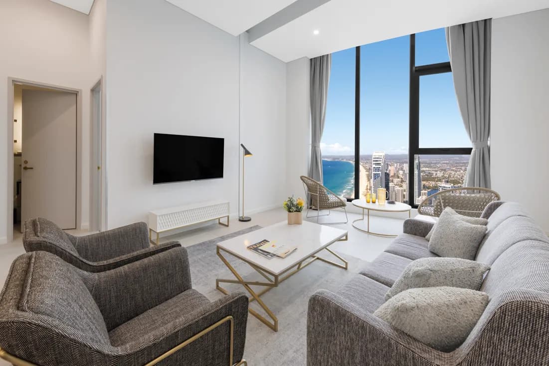 Living area with grey upholstered sofa, two armchairs, coffee table, and large windows showcasing coastal views.
