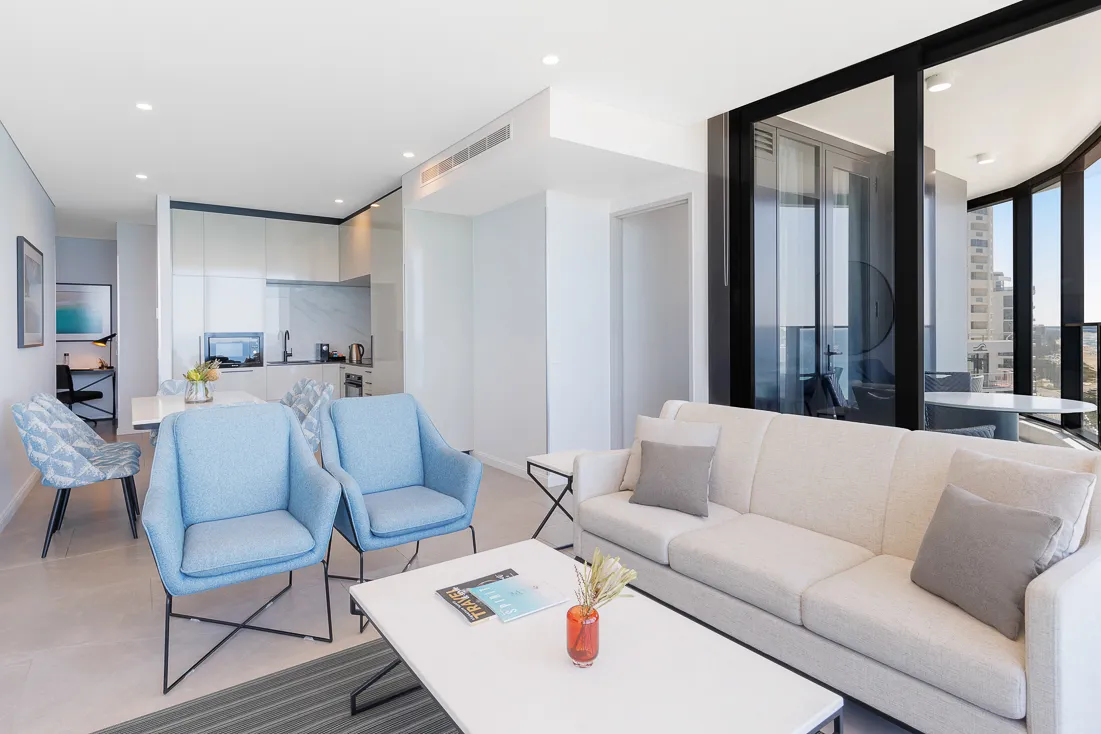 Living area with light blue armchairs, a beige sofa, and a kitchen area in the background.