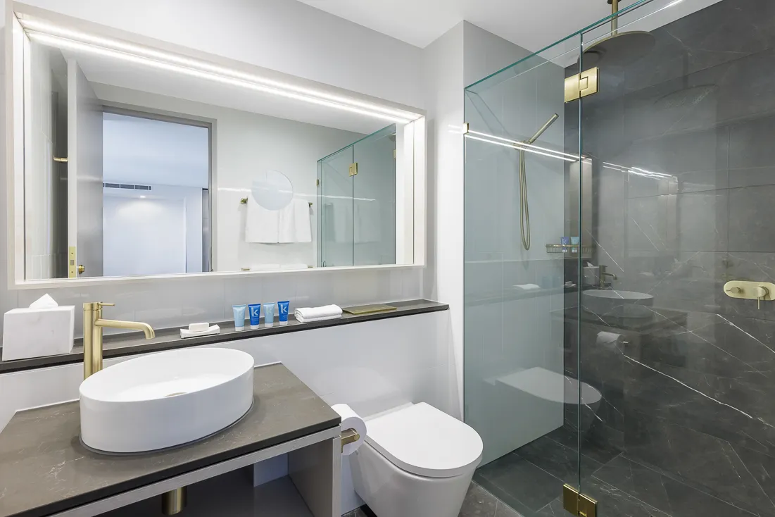 Modern bathroom with a circular mirror, gold fixtures, a white vessel sink, and a glass shower enclosure.