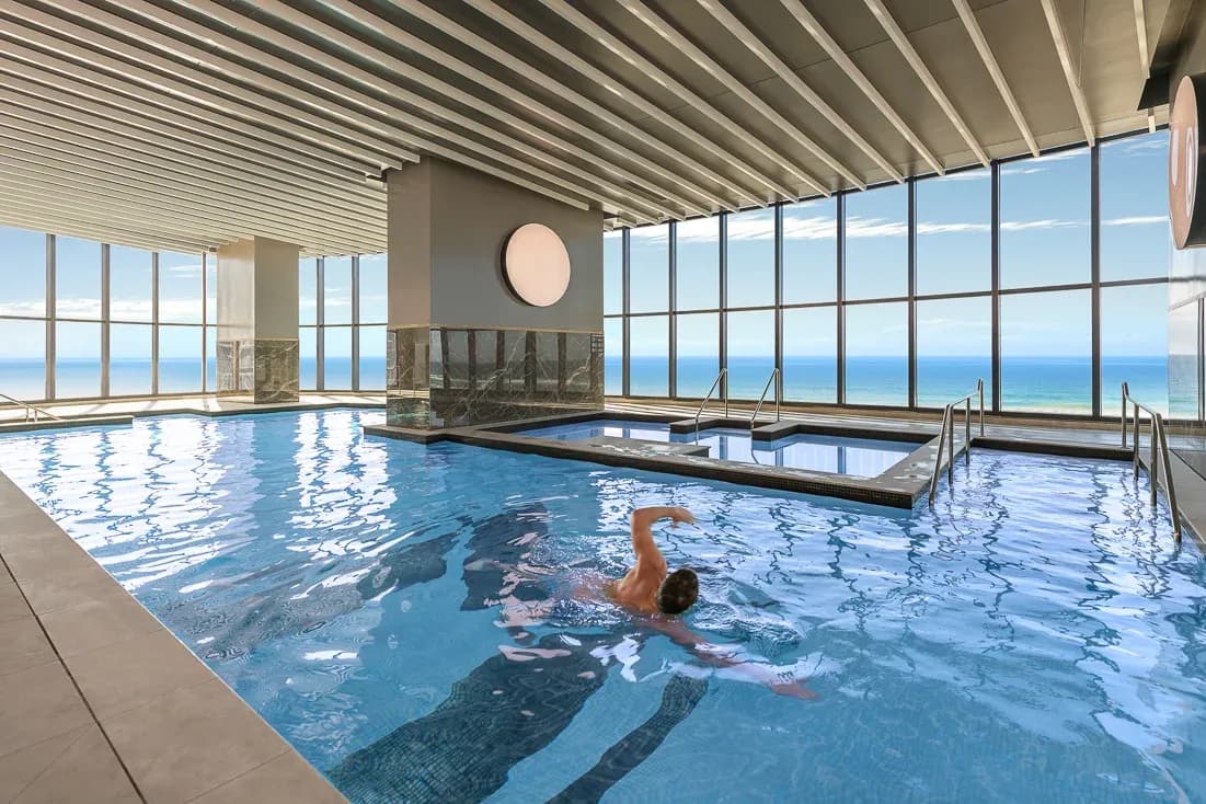 Indoor swimming pool at Meriton Suites Surfers Paradise, featuring large windows with ocean views and a guest swimming.
