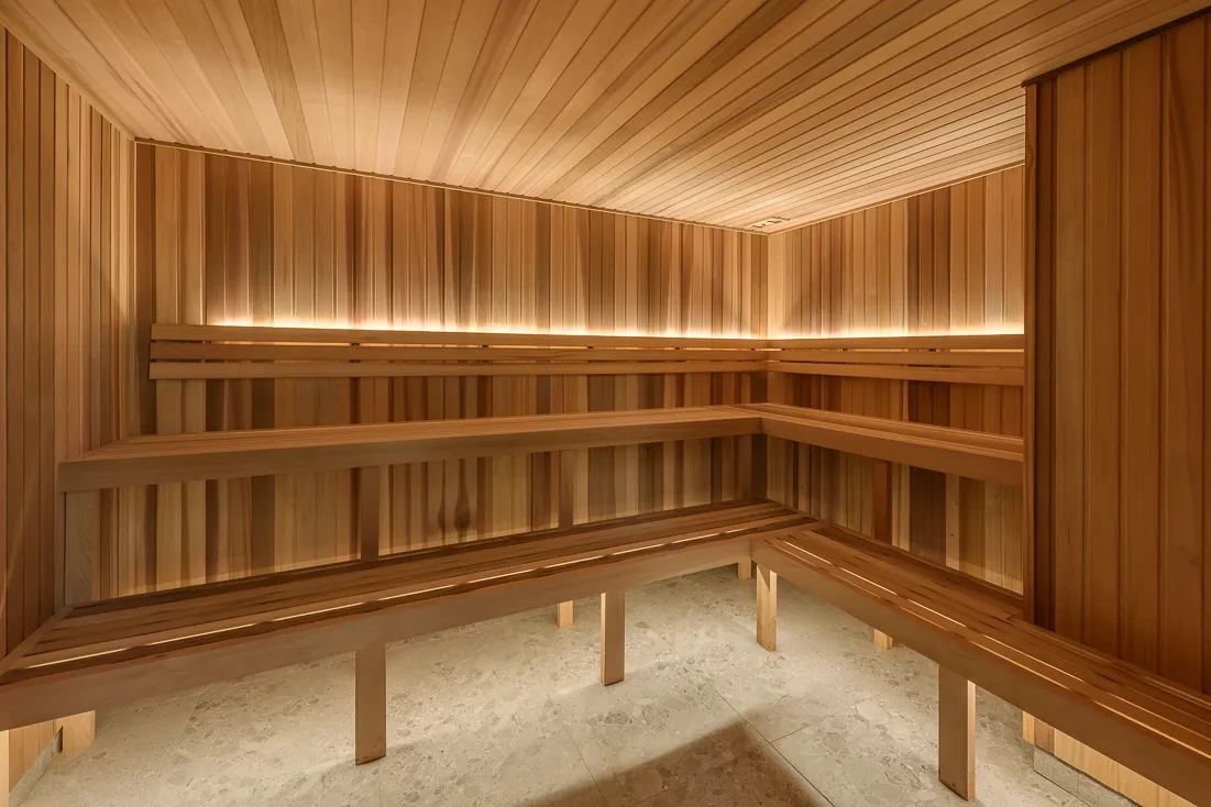 Timber sauna interior featuring slatted wooden benches, warm ambient lighting, and stone flooring.