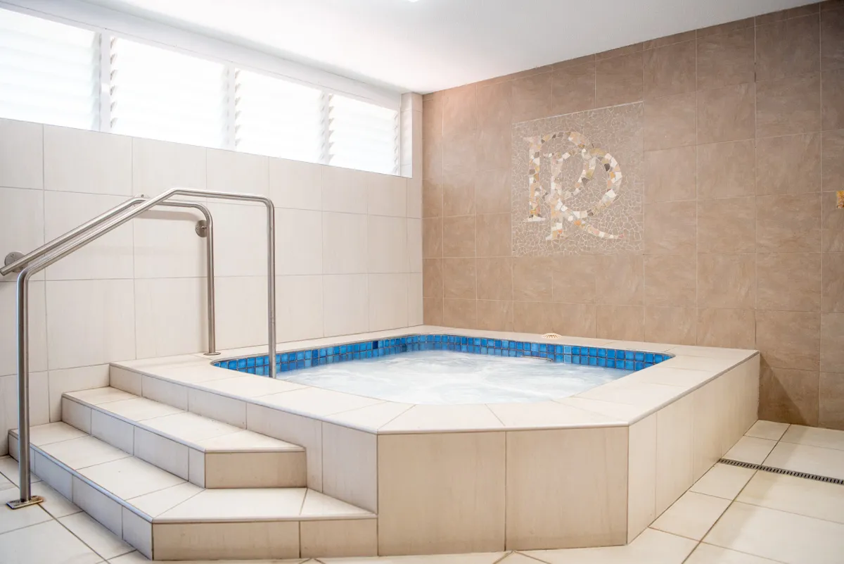 Heated spa pool with blue tiled edge, surrounded by beige tiled walls and a staircase with handrail.