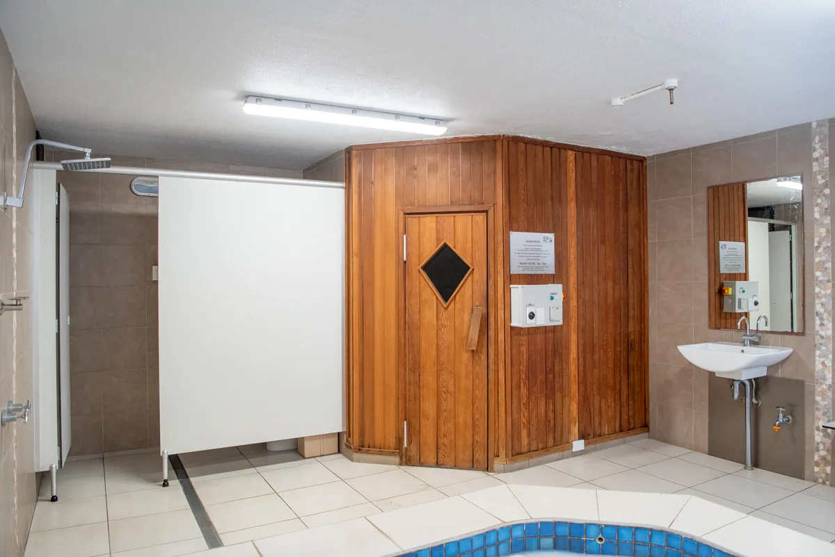 Sauna area featuring a wooden door with a diamond window, tiled floor, and shower facilities.
