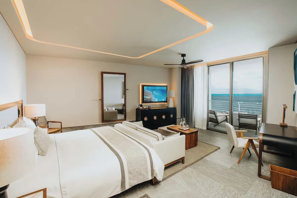 Bedroom with a king-sized bed, a seating area, a television, and large windows offering ocean views.