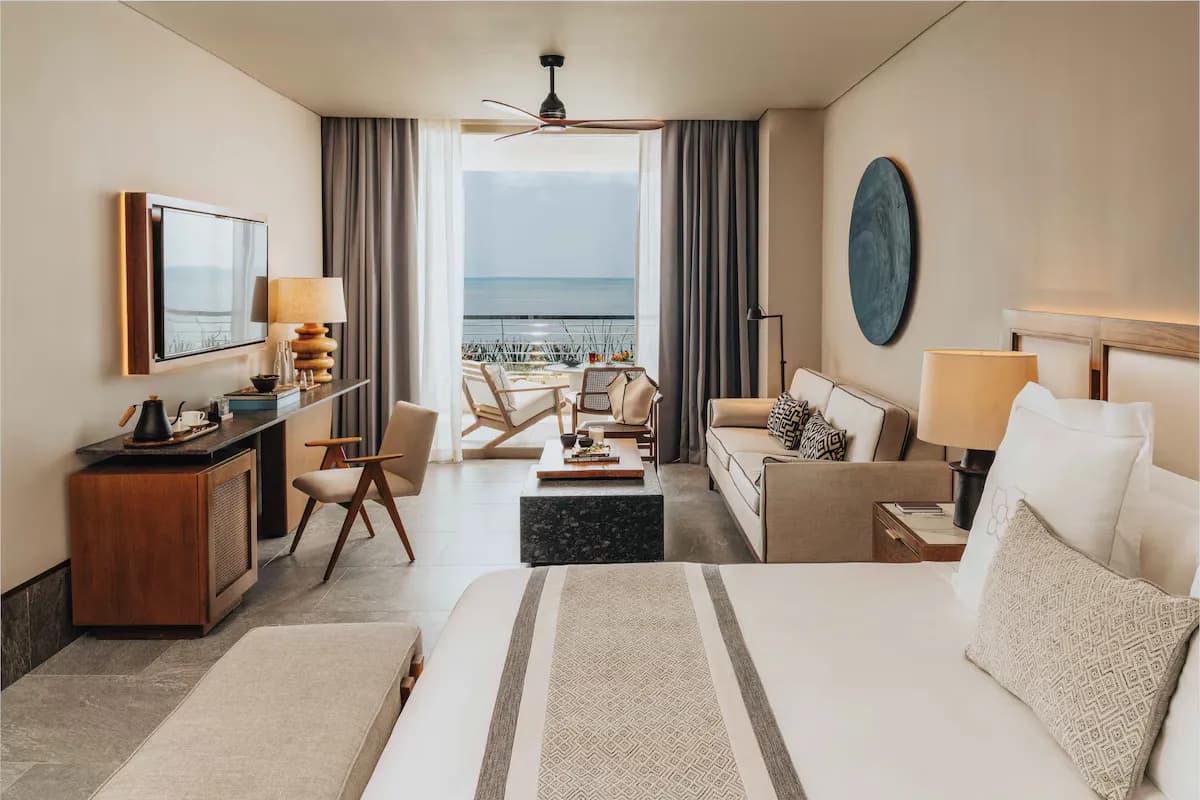 Room interior with a king bed, sitting area, large windows, and ocean view at SHA Mexico.