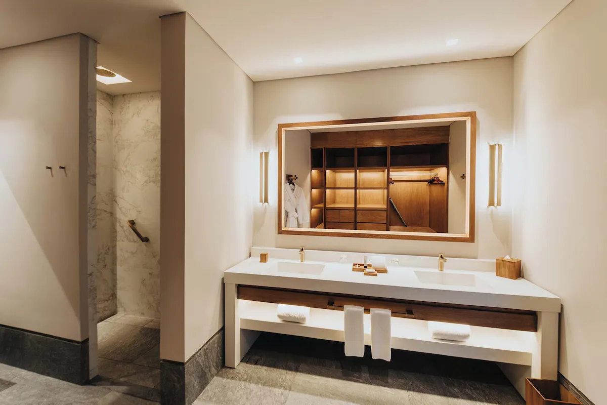 Bathroom interior with dual sinks, wooden cabinetry, a large mirror, and a walk-in shower.