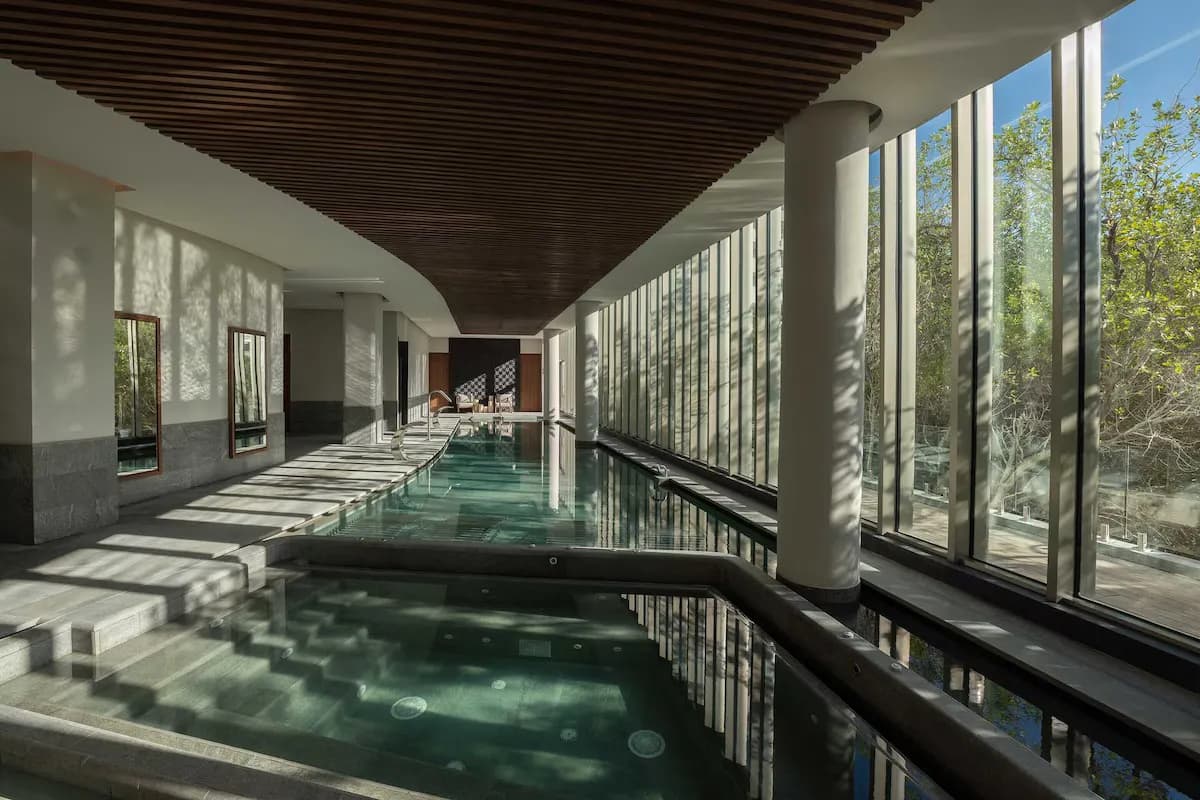Indoor swimming pool and spa with stone steps, large glass windows, and wooden ceiling details at SHA Mexico.