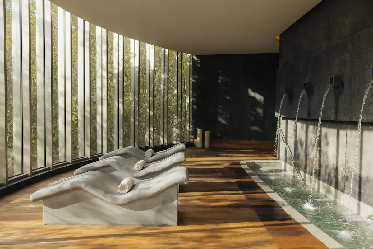 Spa area with curved lounge chairs, wooden flooring, large windows, and a stone wall with water features.
