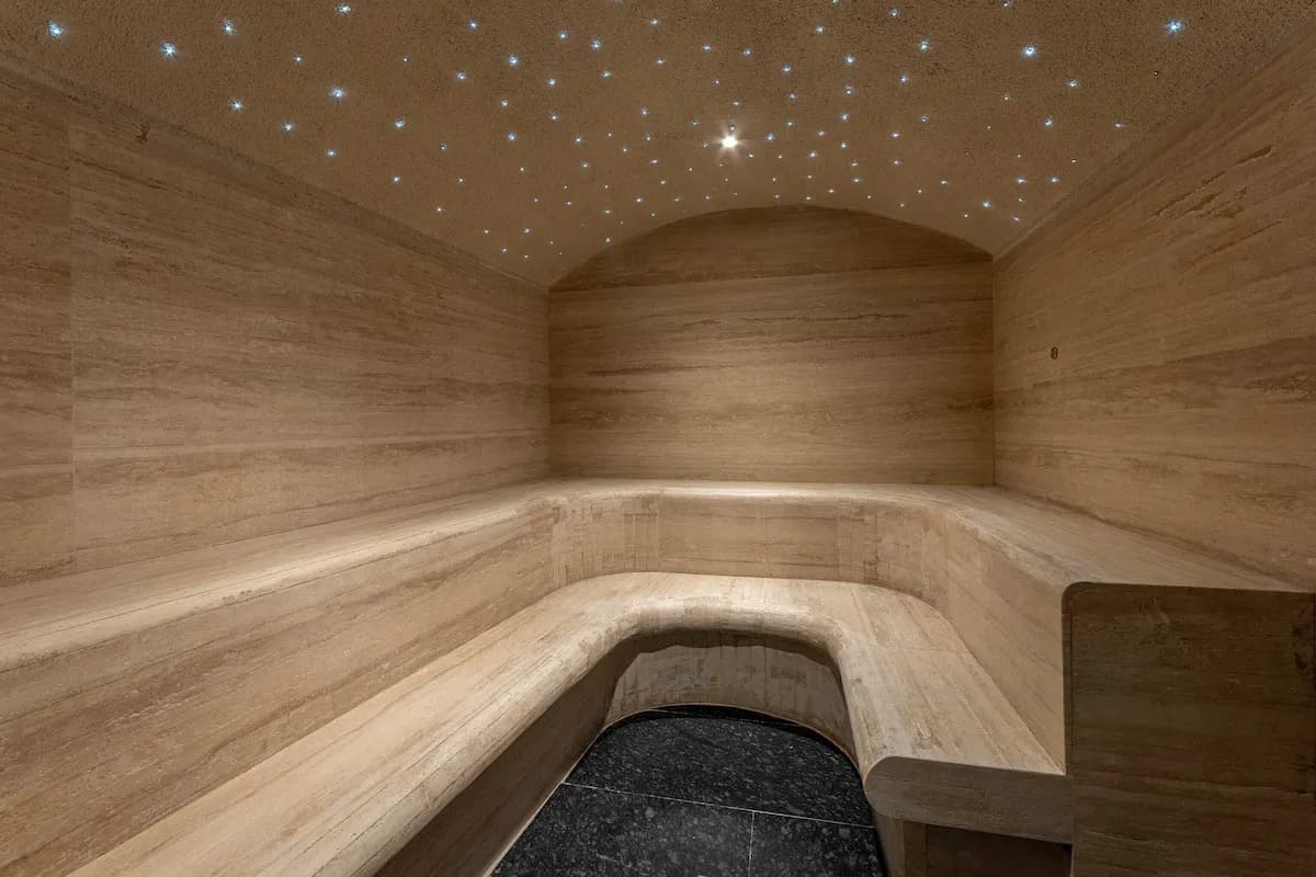 Steam room interior with curved wooden seating, beige stone walls, and a ceiling adorned with small star-like lights.