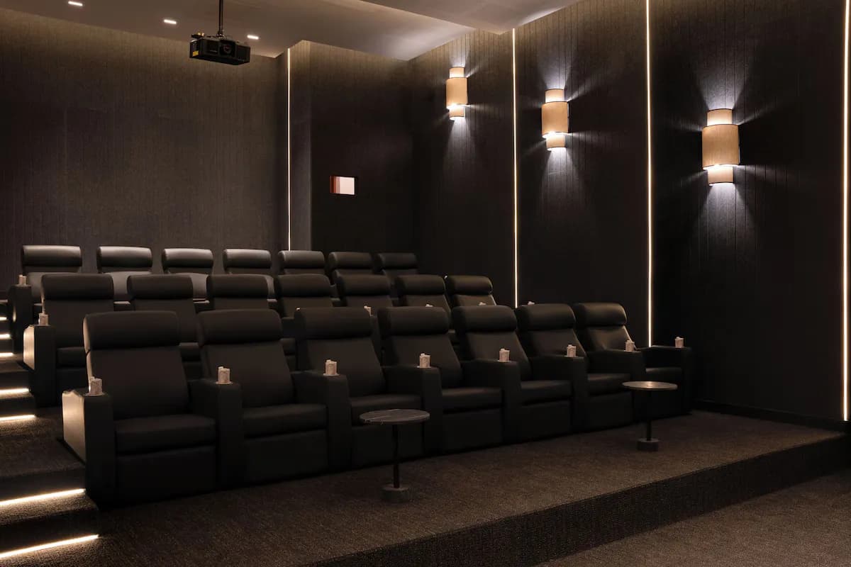 Seating area in a darkened cinema with black recliners, small side tables, and ambient lighting on the walls.