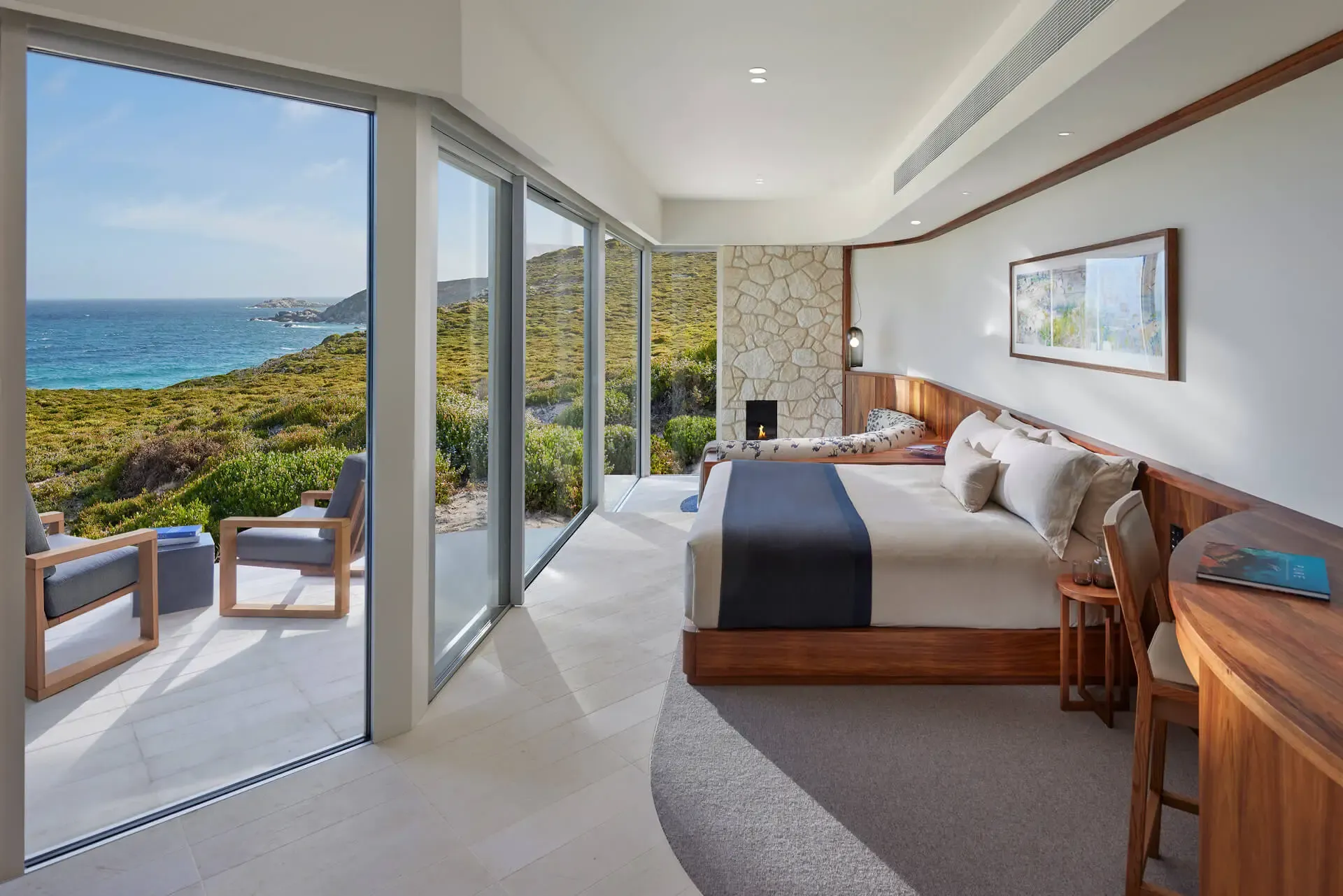 Suite interior featuring a king bed, stone fireplace, and a view of the ocean through glass doors.