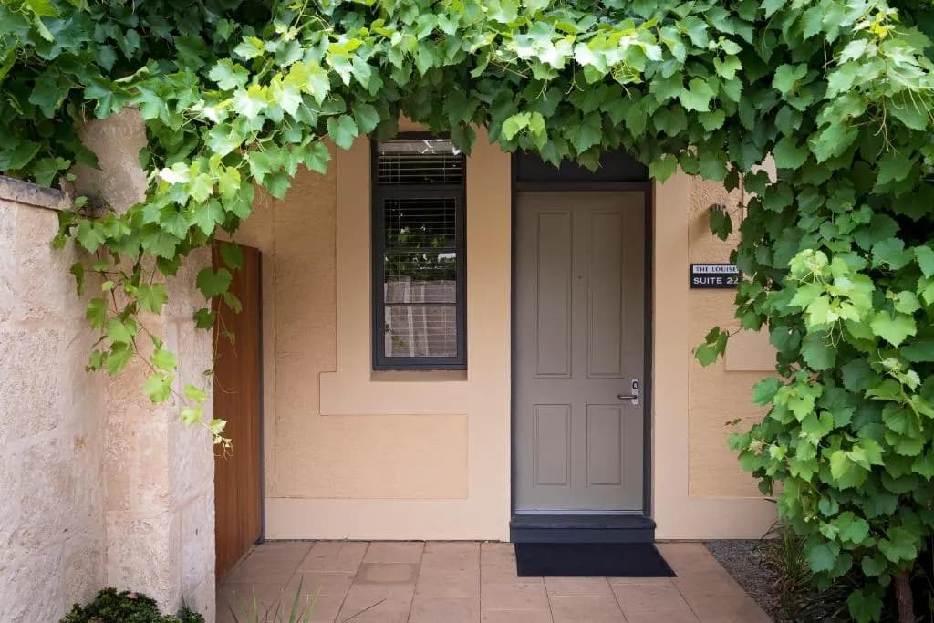Entrance to Suite 22 at The Louise, framed by green grapevines and a stone wall.