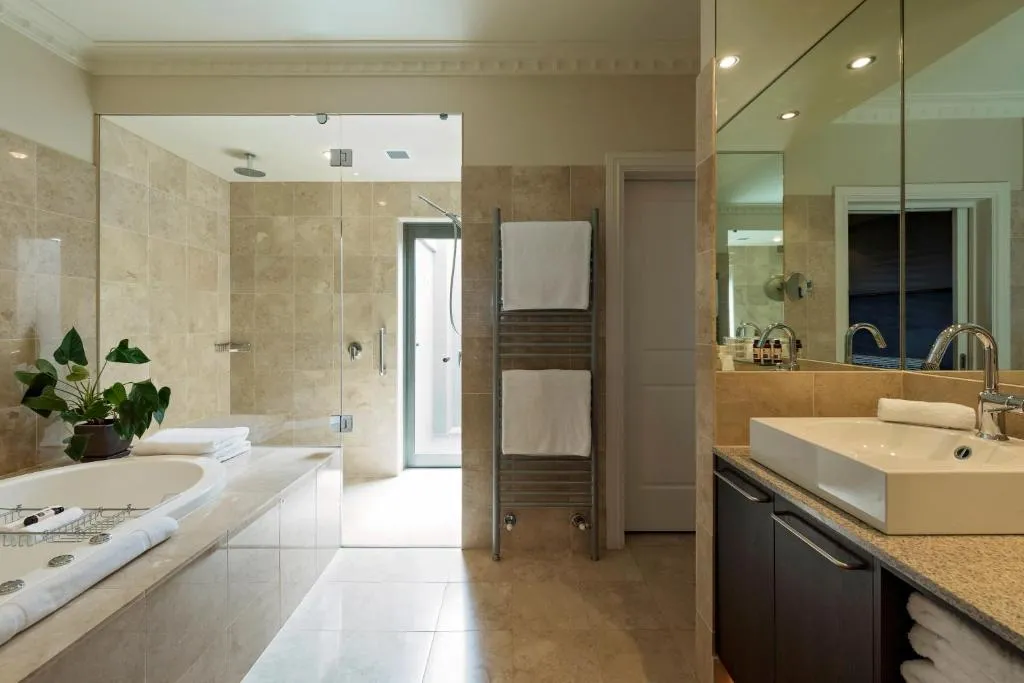 Bathroom with beige tiles, a freestanding bathtub, a glass shower, and a sink with dark cabinetry.