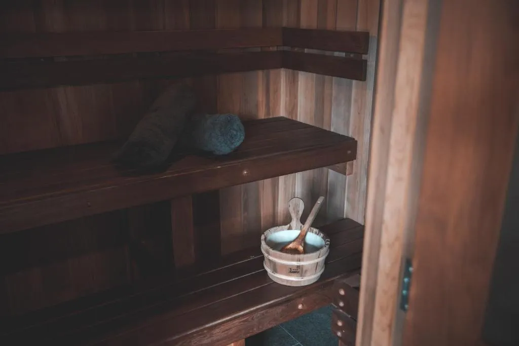 Sauna interior with wooden benches, two rolled towels, and a wooden bucket with a scoop.