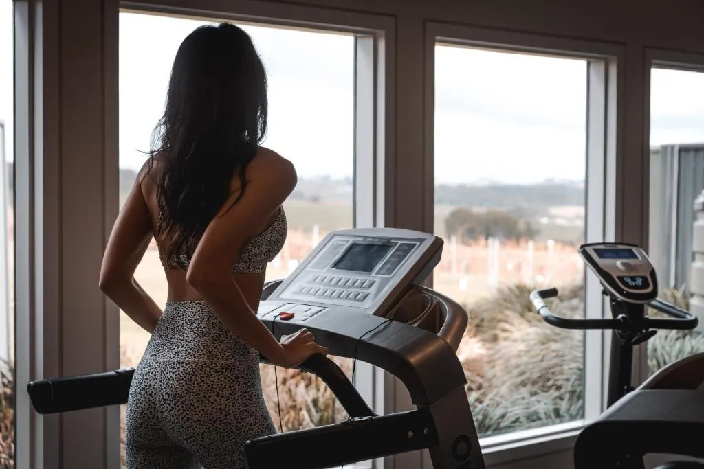 Guest using a treadmill in a gym with large windows overlooking vineyards and distant hills.