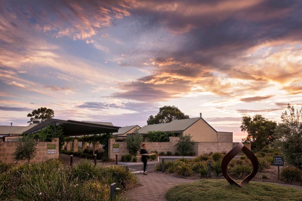 Entrance to The Louise featuring stone walls, a covered walkway, and a modern sculpture under a colorful sky at sunset.