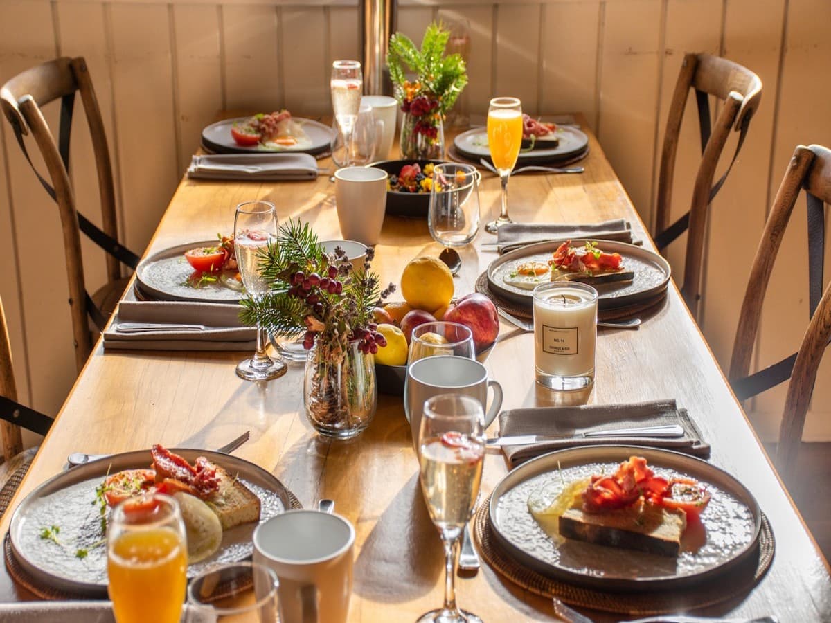 Long timber table at Cross Hill set with bruschetta, fruit, drinks, flowers and warm natural light.