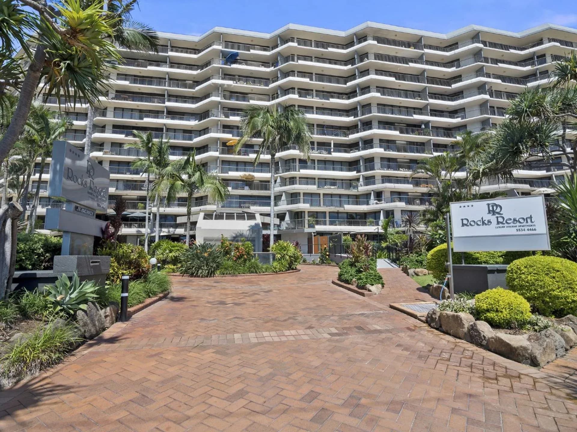 Entrance to The Rocks Resort with landscaped gardens, brick pathway, and a large multi-storey building behind.