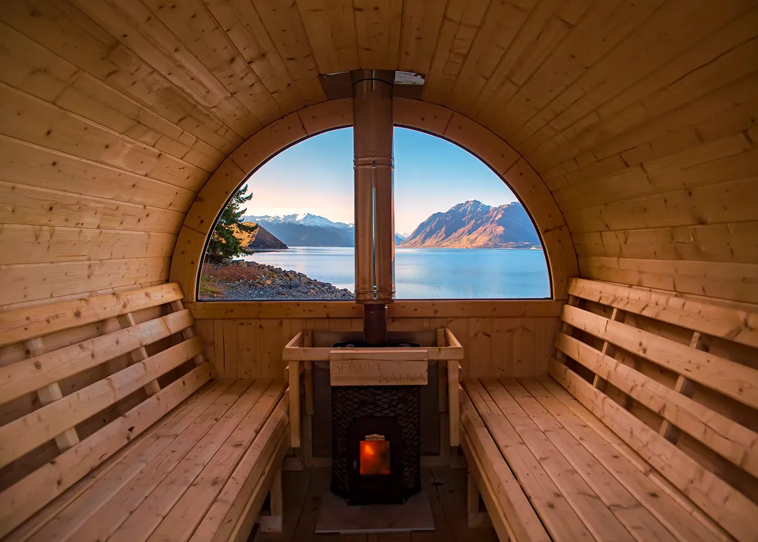 Interior of The Secret Sauna, with timber bench seating, wood-fired stove and views across Lake Hāwea.